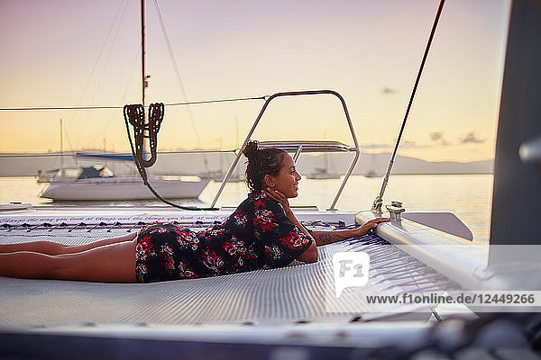 Serene young woman relaxing on catamaran net at sunset