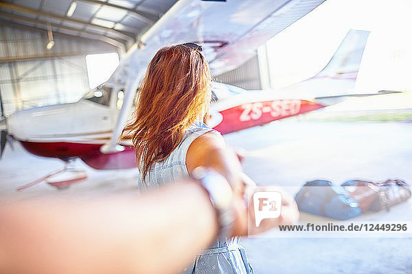 Personal perspective woman leading man by the hand toward small airplane in airplane hangar