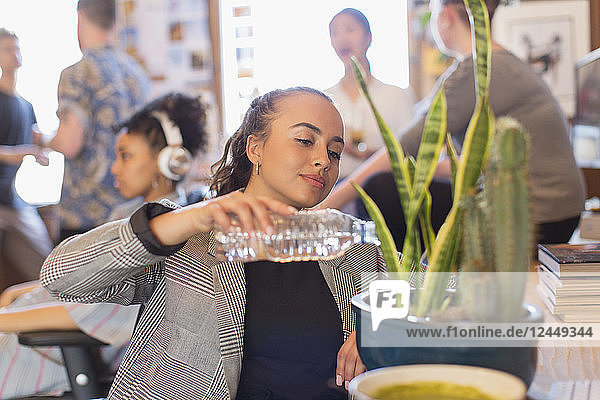 Businesswoman watering cactus plant with bottle water in office