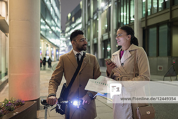 Business people discussing paperwork on urban sidewalk at night