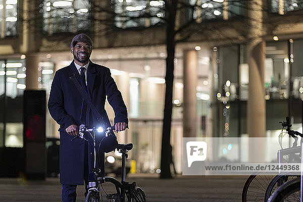 Portrait confident businessman with bicycle on urban street at night