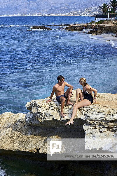Greece  Crete  Chersonissos  couple sitting on rock at beach  holiday