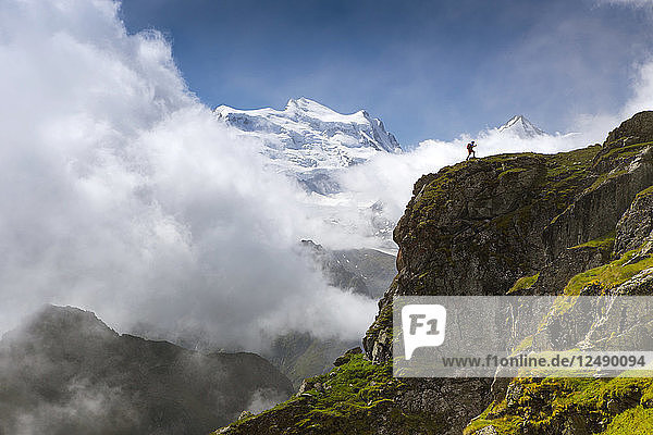 Hiker walking up steep ridge with mountain range in background