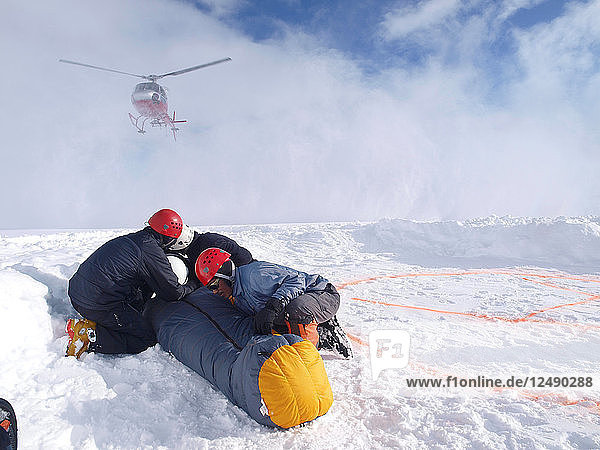Mountain Rescuers are protecting a victim for the down wind of the landing helicopter at 14.000 foot on Denali  formerly known as Mount McKinley.