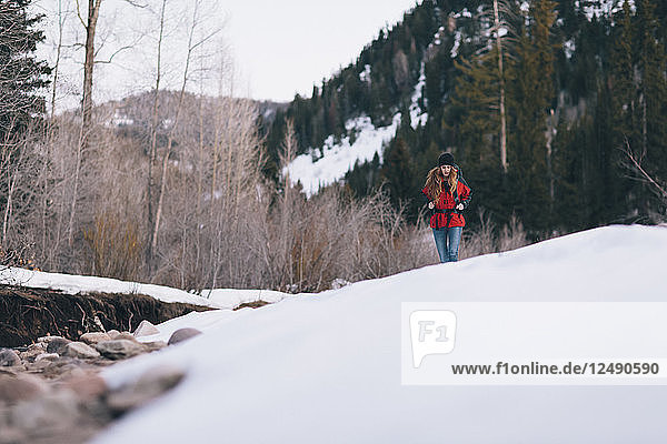Eine junge Frau wandert mit dem Rucksack entlang eines Flusses in den verschneiten Bergen.