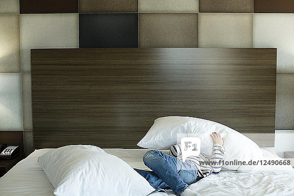 Ein Junge spielt mit einem Kissen in einem Motelzimmerbett.