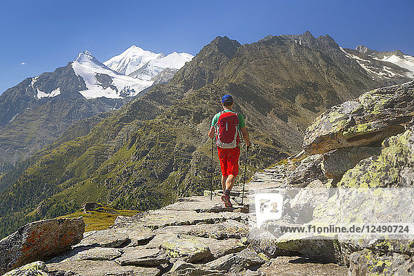 Ein Wanderer auf einem felsigen historischen Handelsweg mit dem Weisshorn über dem Matterhorntal