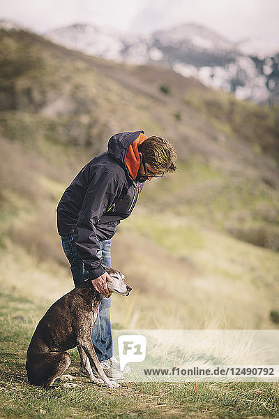 Ein Mann streichelt seinen Hund bei einer Bergwanderung.