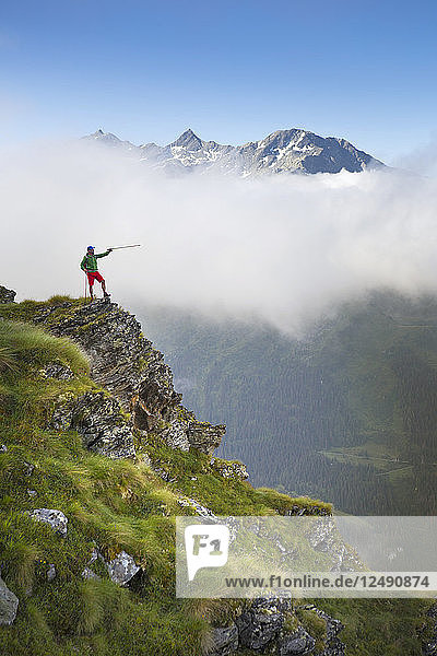 Wanderung auf steilem Grat  mit Wanderstock auf Bergkette im Hintergrund zeigend