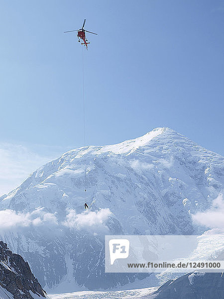 Mountain Ranger hängt an einer langen Leine unter einem Hubschrauber im Denali National Park  Alaska. Der Mount Foraker ist im Hintergrund zu sehen.