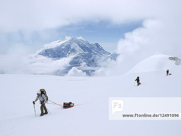 A team of mountaineers are roped up while crossing the upper Kahiltna glacier on their way to 14.000 feet camp Mount McKinley in Alaska. The rope will prevent a climber from falling deep into a crevasse when a snow bridge suddenly collapses. The other team members can then use the rope to rescue the victim. On the sleds the alpinists carry part of their gear  tents and food. Mount McKinley or Denali is the highest mountain peak in North America  with a summit elevation of 20 237 feet (6 168 m) above sea level. At some 18 000 feet (5 500 m)  the base-to-peak rise is considered the largest of any mountain situated entirely above sea level. Measured by topographic prominence  it is the third most prominent peak after Mount Everest and Aconcagua. Located in the Alaska Range in the interior of the U.S. state of Alaska  McKinley is the centerpiece of Denali National Park and Preserve. Mount Hunter is seen in the background.'