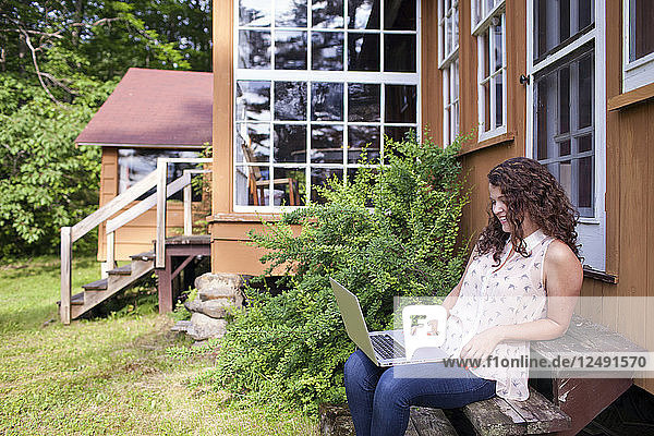Young artist outside of cabin working on laptop