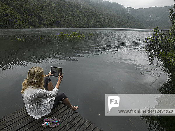 Frau macht Foto mit Tablet auf Steg in Bergsee