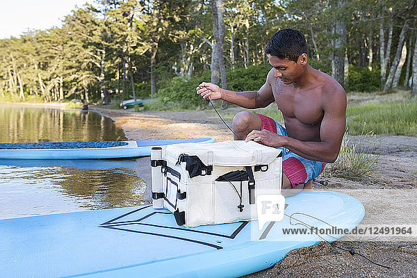 Ein junger Mann  der seine Tackle Box an einem Paddleboard befestigt