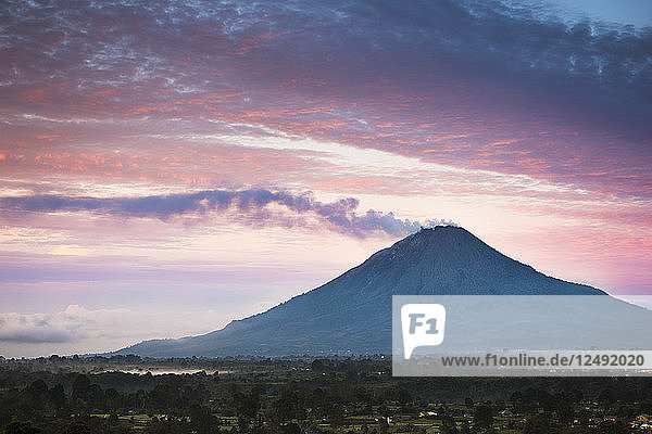 Dampf  der bei Sonnenaufgang vom Mount Sinabung (Gunung Sinabung) aufsteigt. Der Mount Sinabung war 400 Jahre lang ein inaktiver Vulkan und wurde 2010 wieder aktiv.