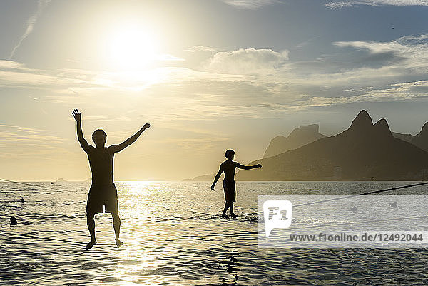Silhouette Of Two Men Balances On A Slackline At Arpoador Beach During The Sunset  Rio De Janeiro  Brazil
