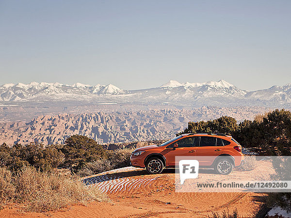 Ein orangefarbenes Auto parkt auf einer Sanddüne  hinter der sich die Wüste ausbreitet.