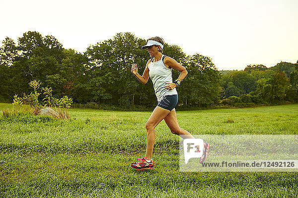 Weibliche Läuferin läuft durch ein Feld an einem nebligen Morgen