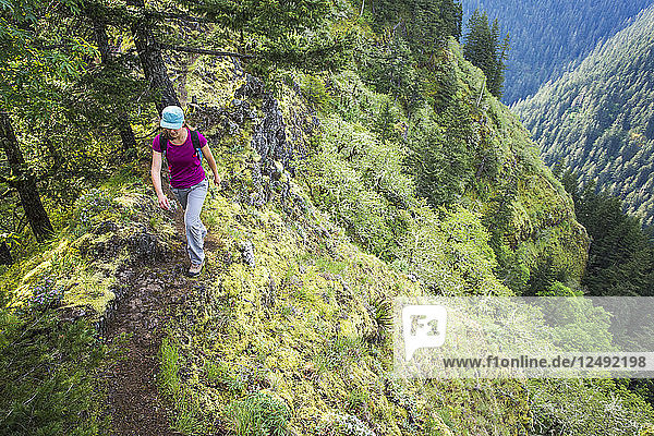 Eine Frau geht auf einem schmalen Pfad mit einem steilen Abstieg in ein grünes Tal unten