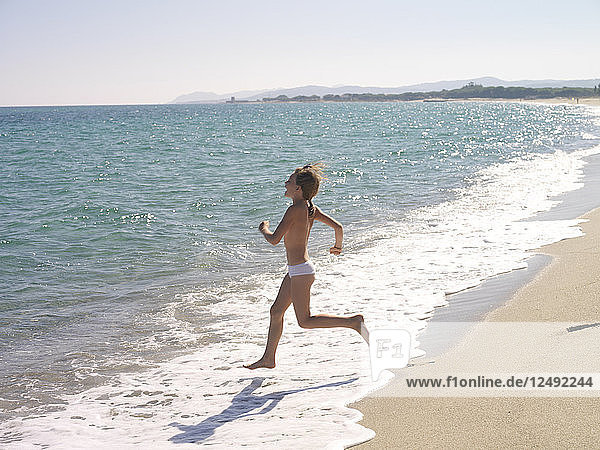 Young girl runs into sea with coastline behind