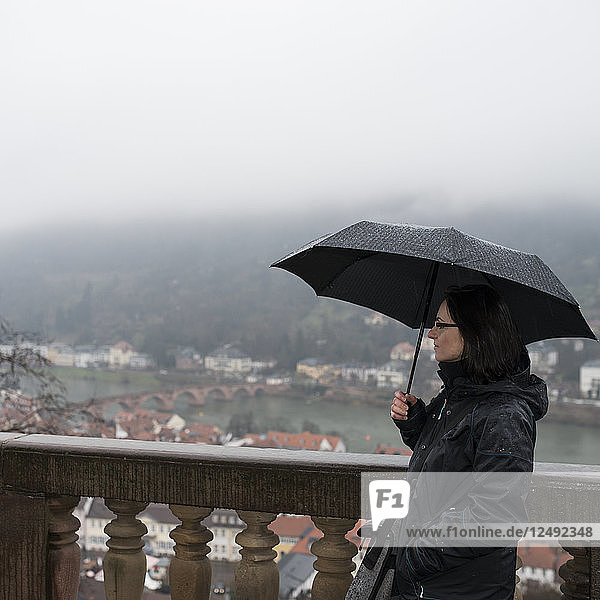 Frau telefoniert oberhalb des Dorfes  unter einem Regenschirm