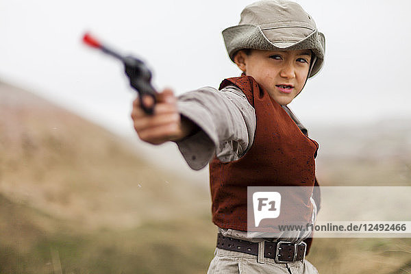 A 6 year old Japanese American boy dressed as an explorer with a hat and vest uses his pistol (six shooter) as he gets ‚Äúbad guys‚Äù as he explores in Badlands National Park  South Dakota.