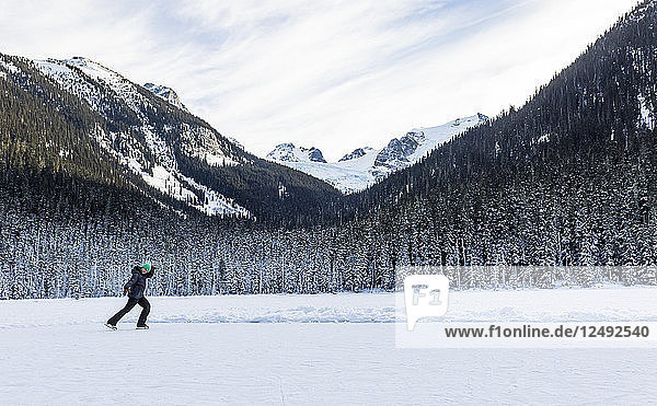 Ein Mädchen läuft an einem kalten Wintertag auf dem Joffre Lake in British Columbia Schlittschuh