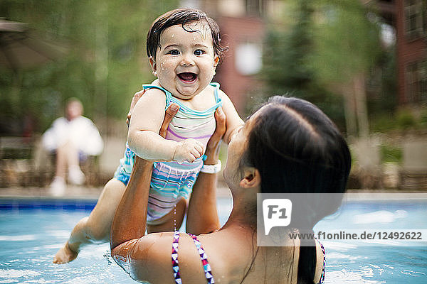 A Japanese American mother swims and holds her 10 month old baby girl in a swimming pool.