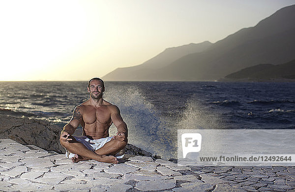 Muskulöser Mann meditiert in einer Yoga-Pose  in der Nähe des Meeres. Ka?ü Antalya Türkei