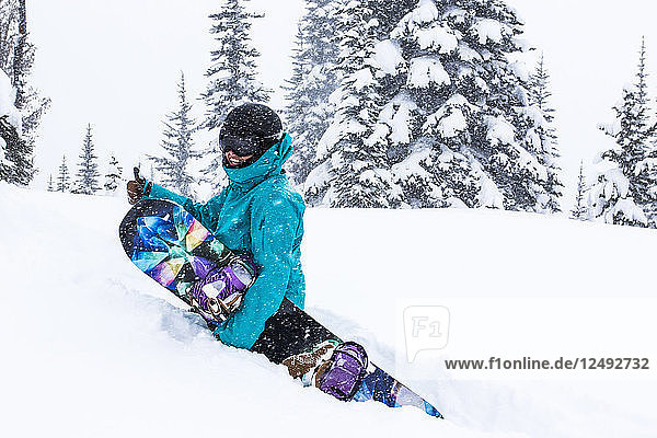 Ein weiblicher Snowboarder wandert durch hüfttiefen Schnee und gibt einen Daumen hoch im Whistler Blackcomb Ski Resort