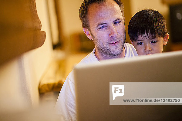Ein Mann hält einen vierjährigen japanisch-amerikanischen Jungen im Arm  während sie beide auf einen Laptop schauen.