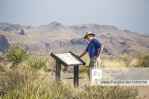 Ein Mann  der in einer Wüstenlandschaft steht und auf ein Hinweisschild schaut