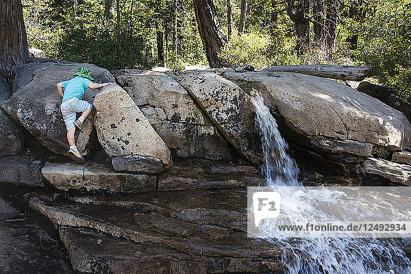 Toddler boy climbs rocks next to waterfall on way to Horsetail Falls  Strawberry  California.