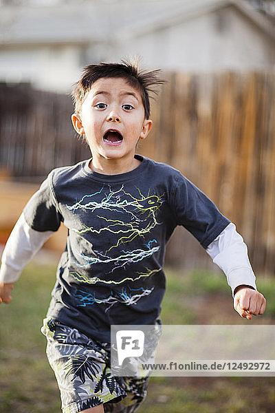 A 6 year old Japanese American boy run through the backyard.