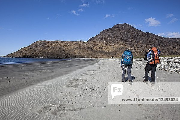Ein Bergsteigerpaar schlendert über den Strand zum Start der Route