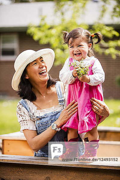 Eine japanisch-amerikanische Mutter und ihr 1 Jahr altes kleines Mädchen pflanzen einen Garten in Pflanzkästen.