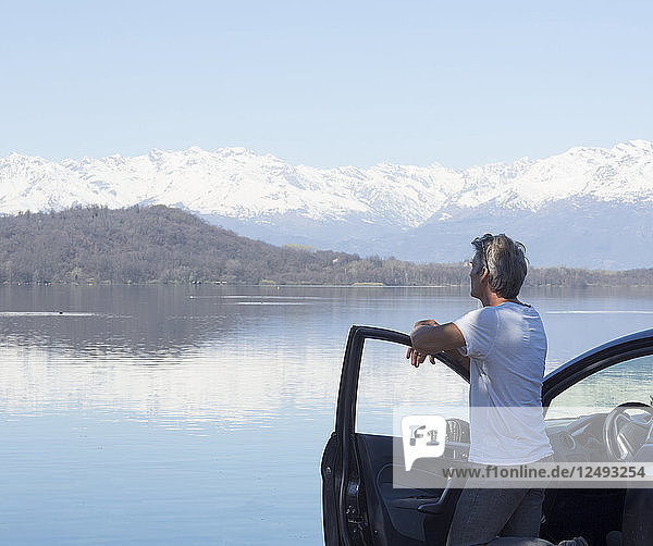 Älterer Mann entspannt sich auf der Tür eines Autos am See