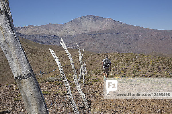 View past wooden fence posts to hiker on desert trail in mountains