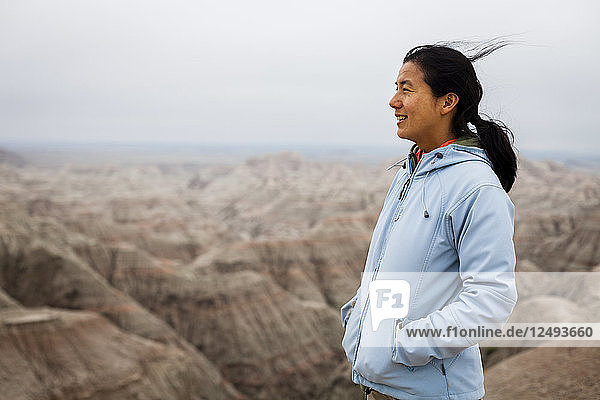 Eine japanische Amerikanerin steht an einem Beobachtungsposten  hinter ihr erstrecken sich die klassischen Felsformationen (Zinnen und Türme) im Badlands National Park  South Dakota.