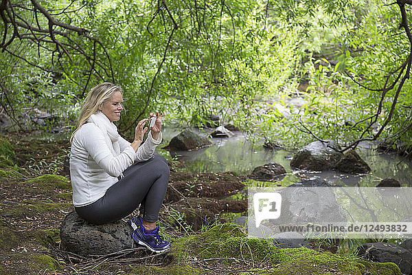 Frau entspannt sich im grünen Wald und macht ein Foto mit ihrem Smartphone