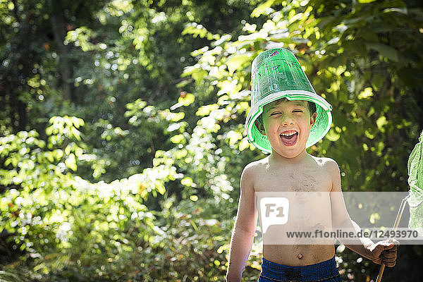 Toddler boy jokes with a bucket on his head and butterfly net in hand while next to creek in Bidwell Park  Chico  California.