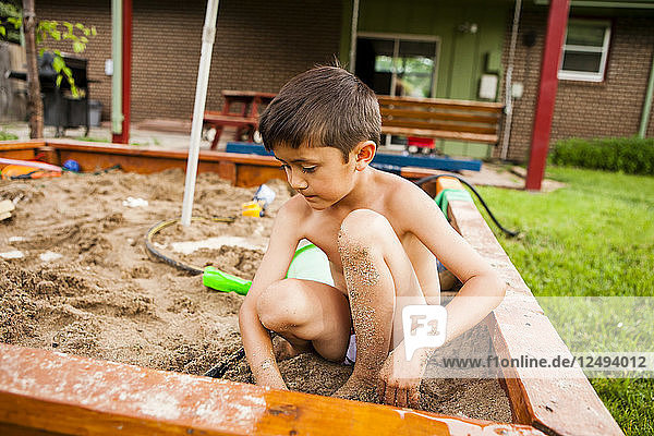 Ein 6-jähriger japanisch-amerikanischer Junge spielt mit einem Schlauch in einem Sandkasten.