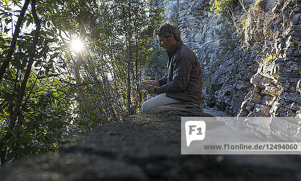 Mann prüft Tablette an Felswand am Weg