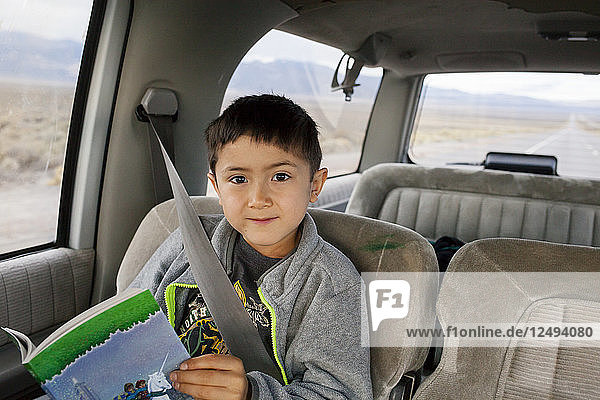 A seven year old boy sits and reads in a suburban on a road trip across Nevada.