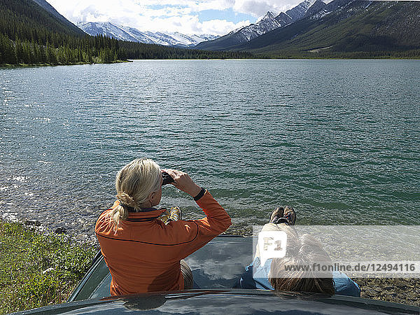 Ein Paar sitzt auf der Motorhaube eines Lastwagens und benutzt ein Fernglas über dem See