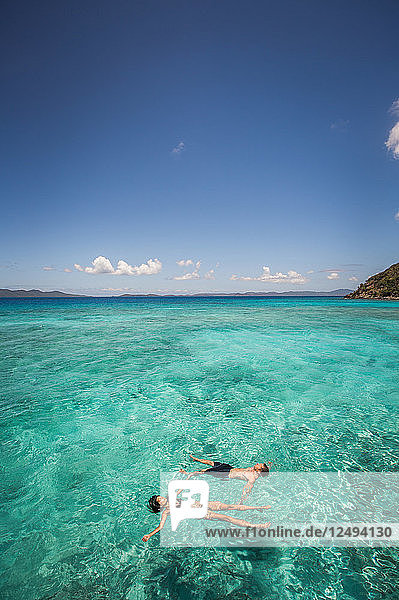 Ein Pärchen schwimmt auf dem Rücken im klaren  türkisfarbenen Karibikwasser.