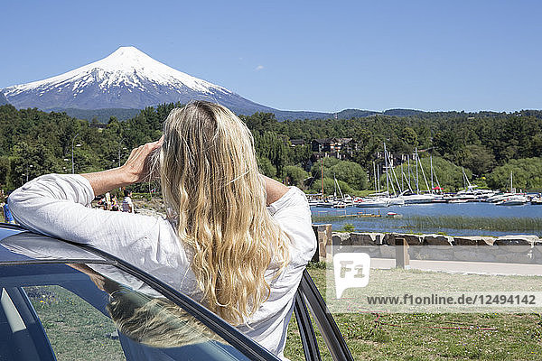 Woman leans against car and takes photo of snow capped volcano