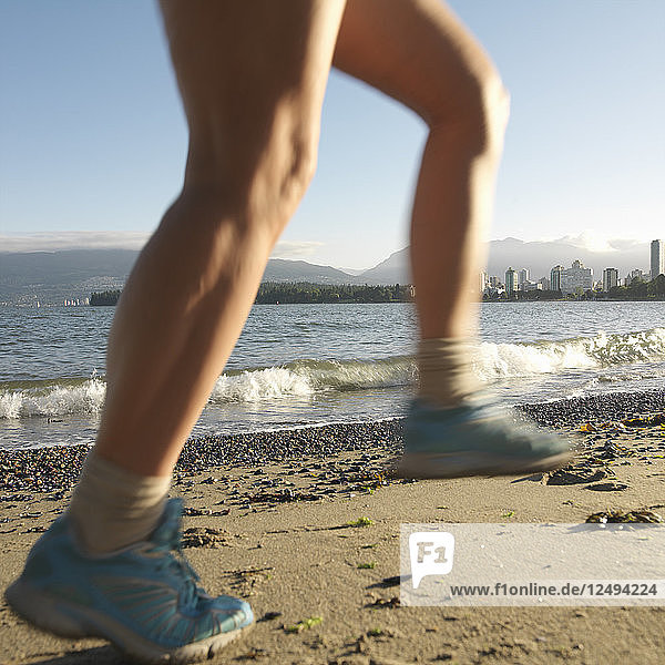Detail von Frauen Beinen laufen am Strand mit Skyline hinter