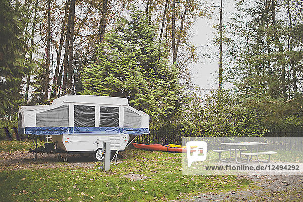 Ein Zeltanhänger  zwei Kajaks und ein Picknicktisch auf einem örtlichen Campingplatz.
