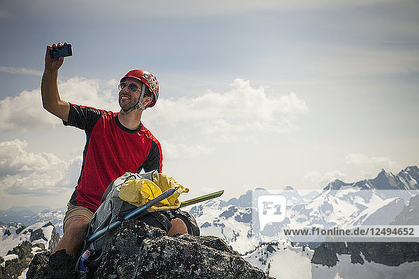 A climber takes a selfie with his smartphone from the summit of Trio Peak in British Columbia  Canada.